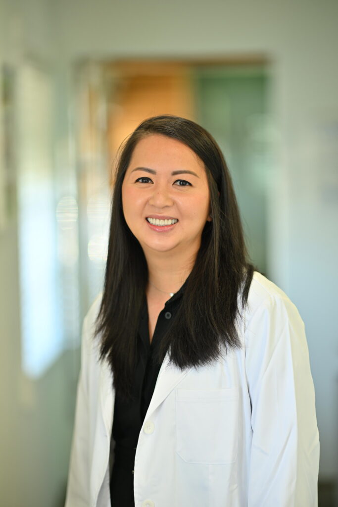 Professional headshot of Annie Hsu, smiling warmly in a white lab coat at Wellbeing Dentistry.