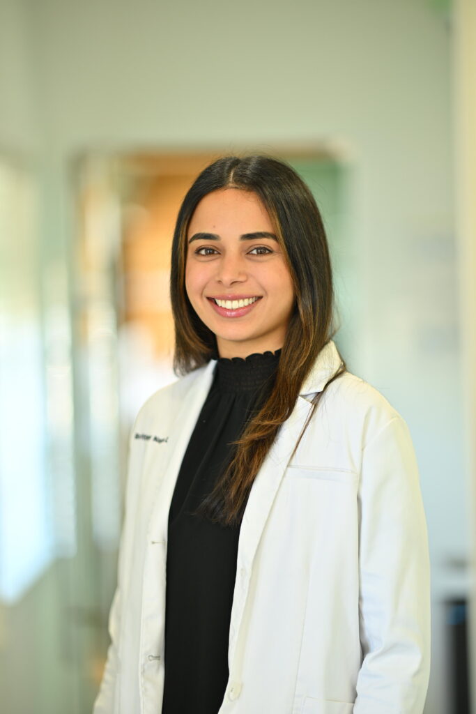 Professional headshot of Brittany Nagra, smiling warmly in a white lab coat at Wellbeing Dentistry.