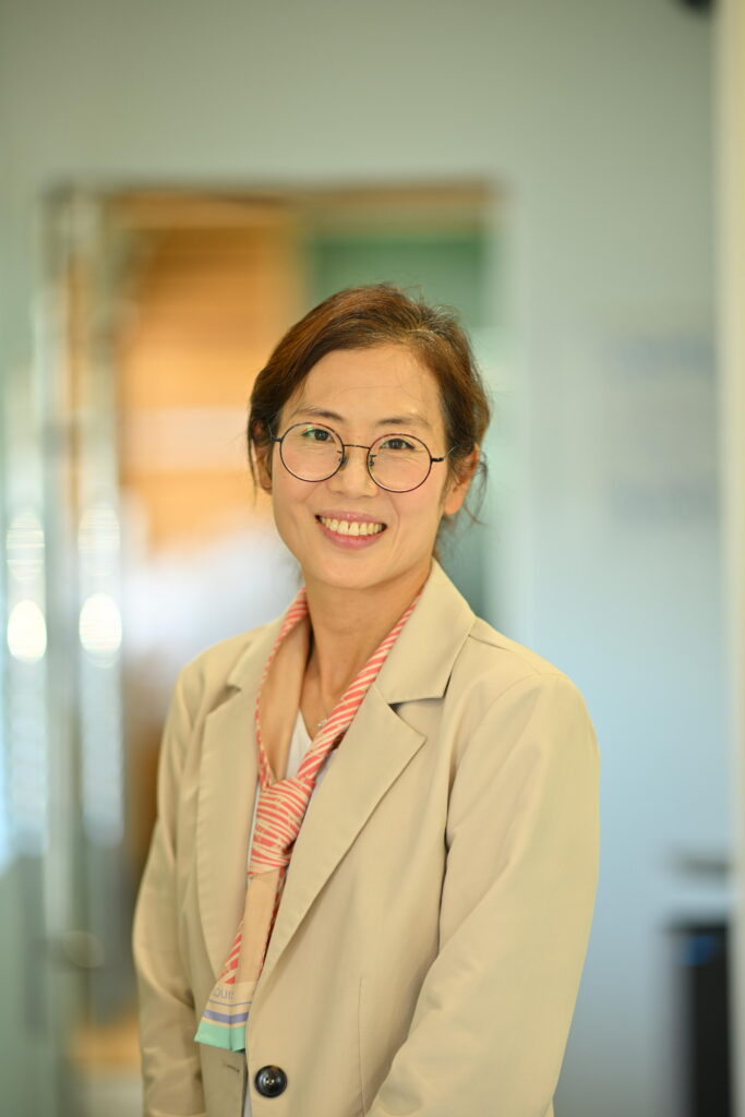 Professional headshot of Crystal Lee, smiling warmly in a blazer and scarf at Wellbeing Dentistry.