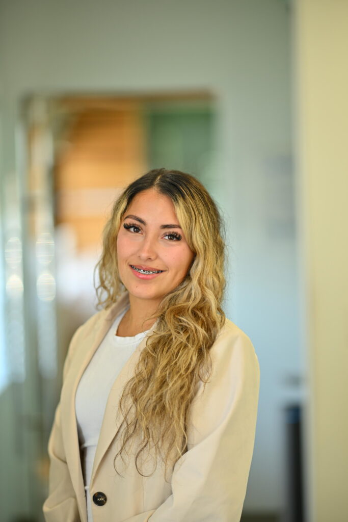 Professional headshot of Giselle Ortiz, smiling warmly in a beige blazer at Wellbeing Dentistry.