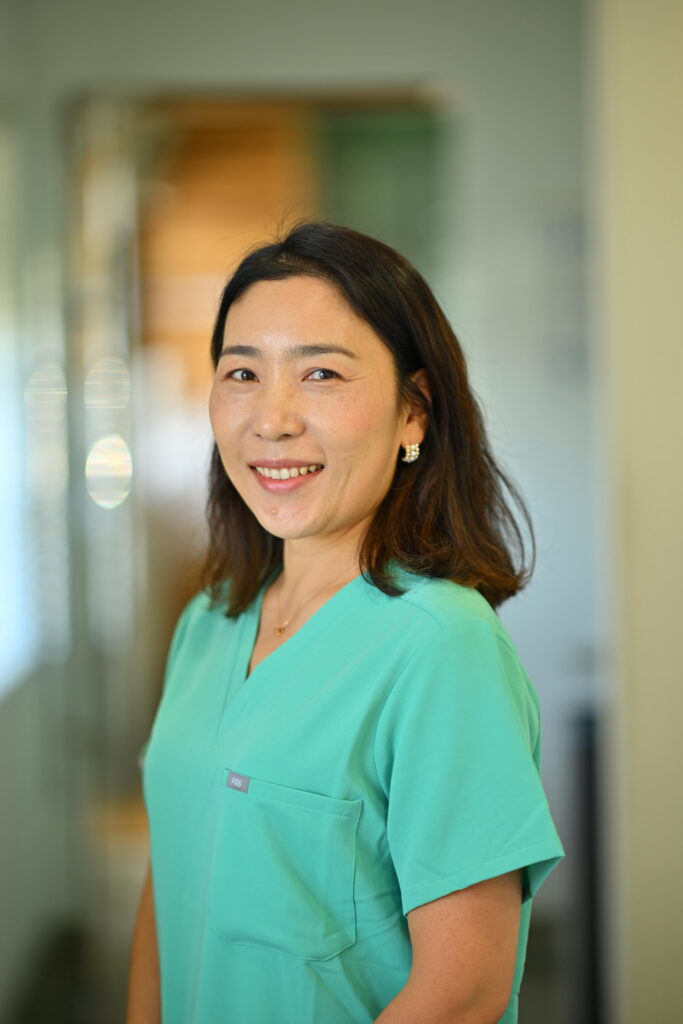 Professional headshot of Hana Chung, smiling warmly in green scrubs at Wellbeing Dentistry.