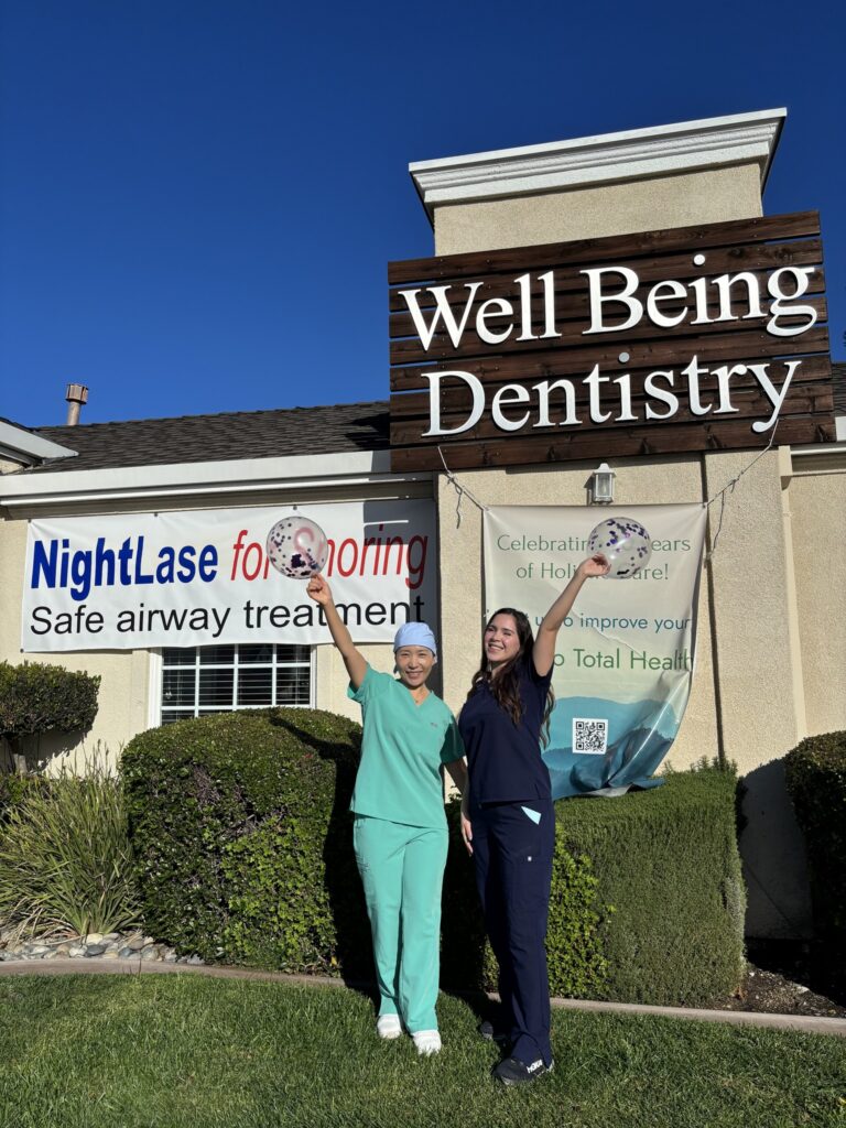 Two Wellbeing Dentistry team members standing in front of the practice sign, which highlights NightLase for snoring and safe airway treatment in Santa Clara.