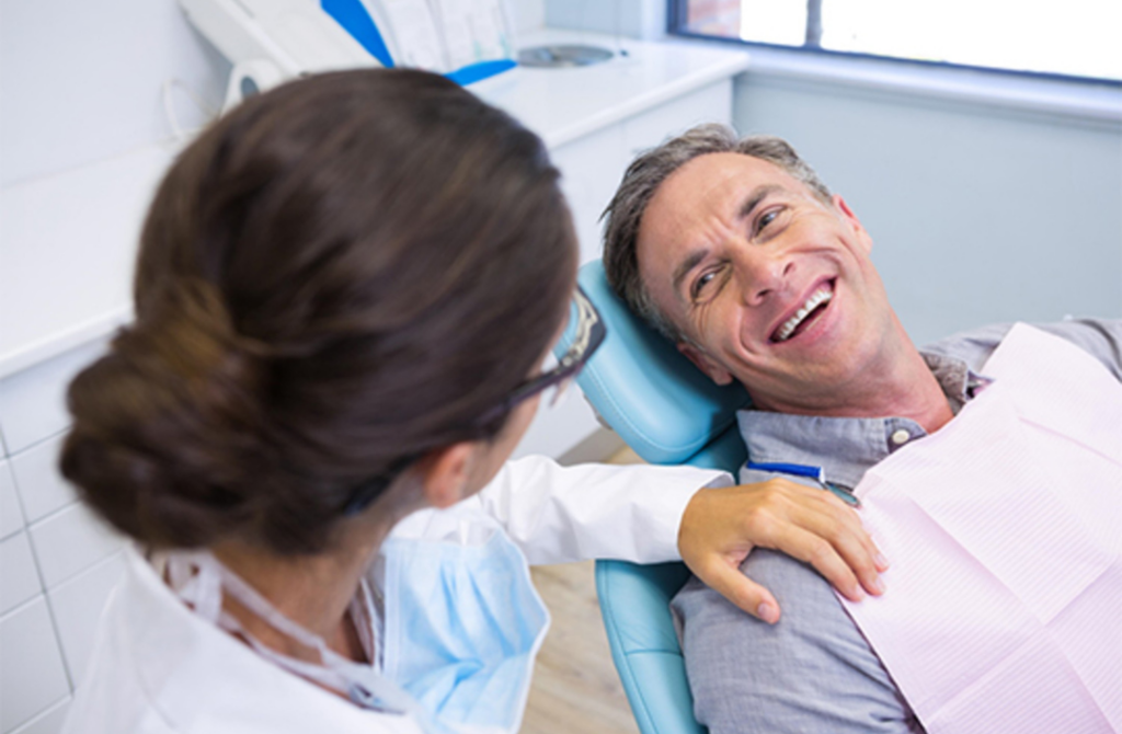 A smiling patient at Wellbeing Dentistry 3.0 discussing biological ozone therapy with a female dental professional in a bright, modern clinical setting.