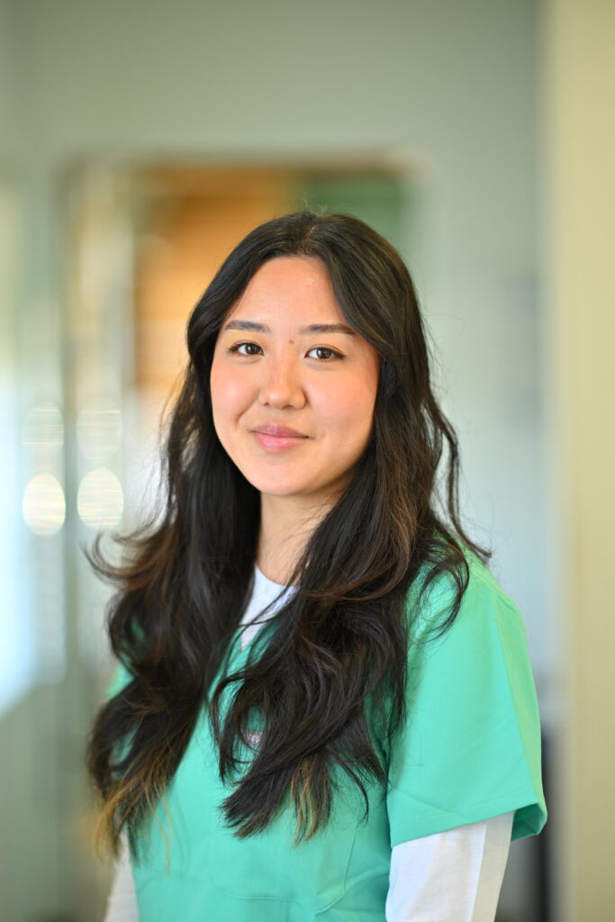 Professional headshot of Rachel Yi, smiling gently in green scrubs at Wellbeing Dentistry.