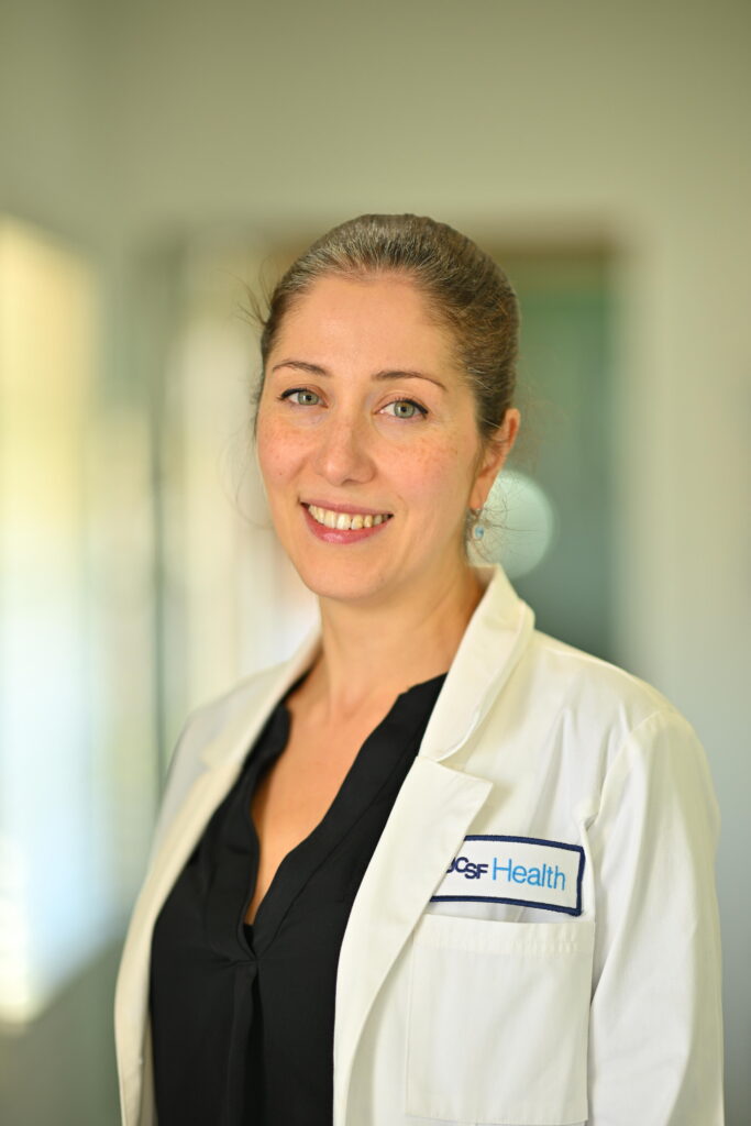 Professional headshot of Roya Rad, smiling brightly in a white lab coat at Wellbeing Dentistry.