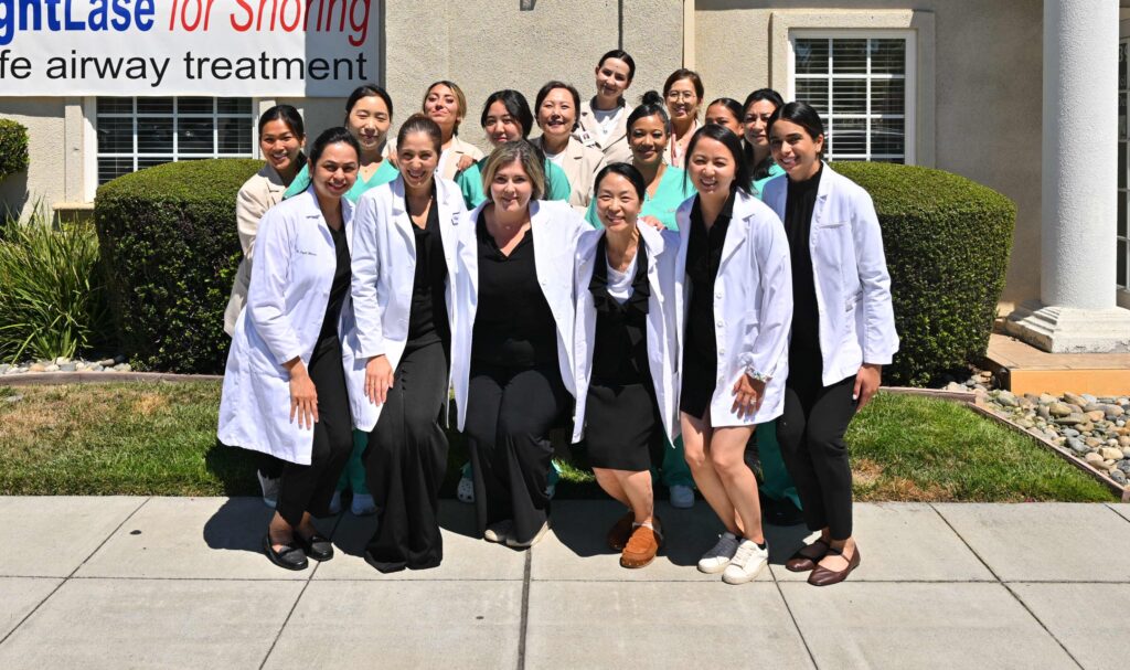 The full professional team at Wellbeing Dentistry, dressed in scrubs and lab coats, smiling together outside the practice.